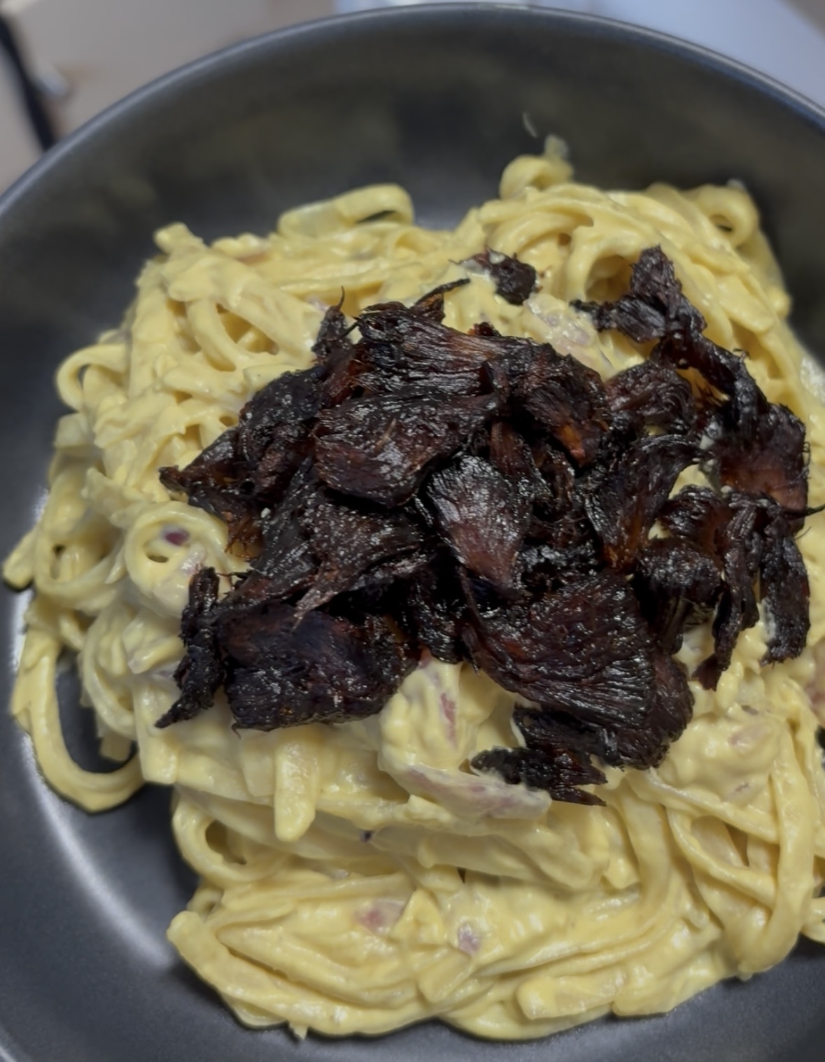 A bowl of creamy vegan carbonara with gluten-free fettuccine, topped with crispy Lion's Mane mushroom bacon.